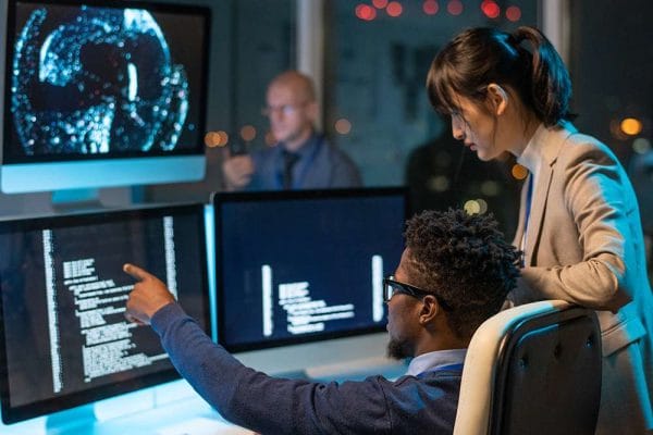 AI for DevOps: Developers collaborating on code. Team working with AI on multiple computer screens.