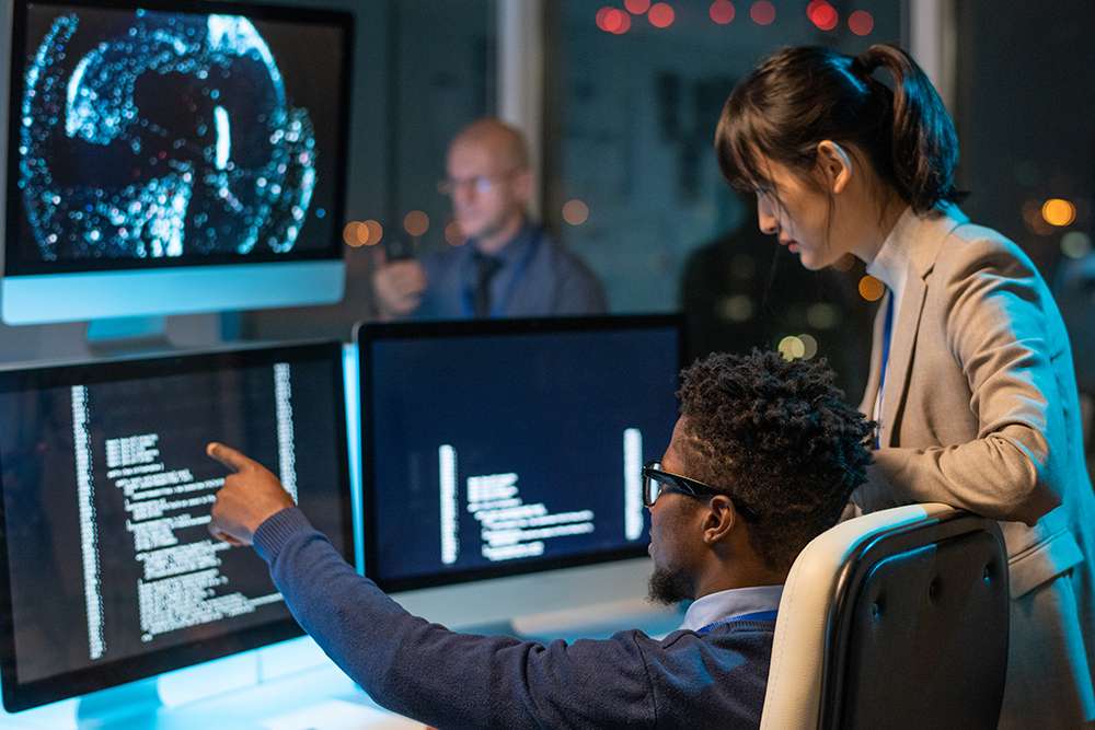 AI for DevOps: Developers collaborating on code. Team working with AI on multiple computer screens.