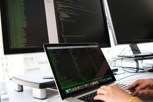 Core DevOps Skills: Developer coding on laptop with dual monitors.