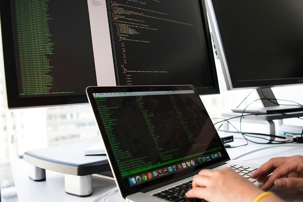 Core DevOps Skills: Developer coding on laptop with dual monitors.