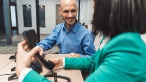 Customer service representative hands phone to smiling customer. Office setting.