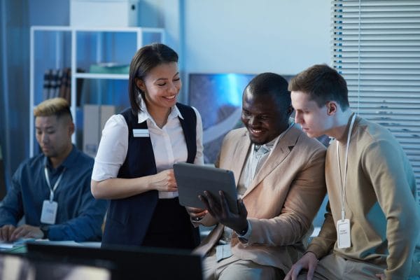 Customer Success Manager journey: Team collaborating, looking at tablet. Diverse group in office setting.