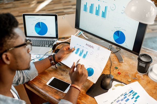 Data Analytics Specialist reviewing charts. Graphs on screen, data analysis in progress.