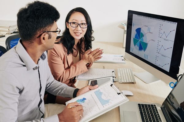 Data Science Foundations: Two analysts review charts and graphs on a computer and clipboard.