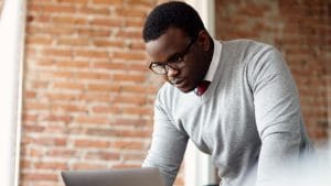 Business Studies: Adult student with laptop. Man in glasses studying business, brick wall background.