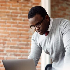 Business Studies: Adult student with laptop. Man in glasses studying business, brick wall background.