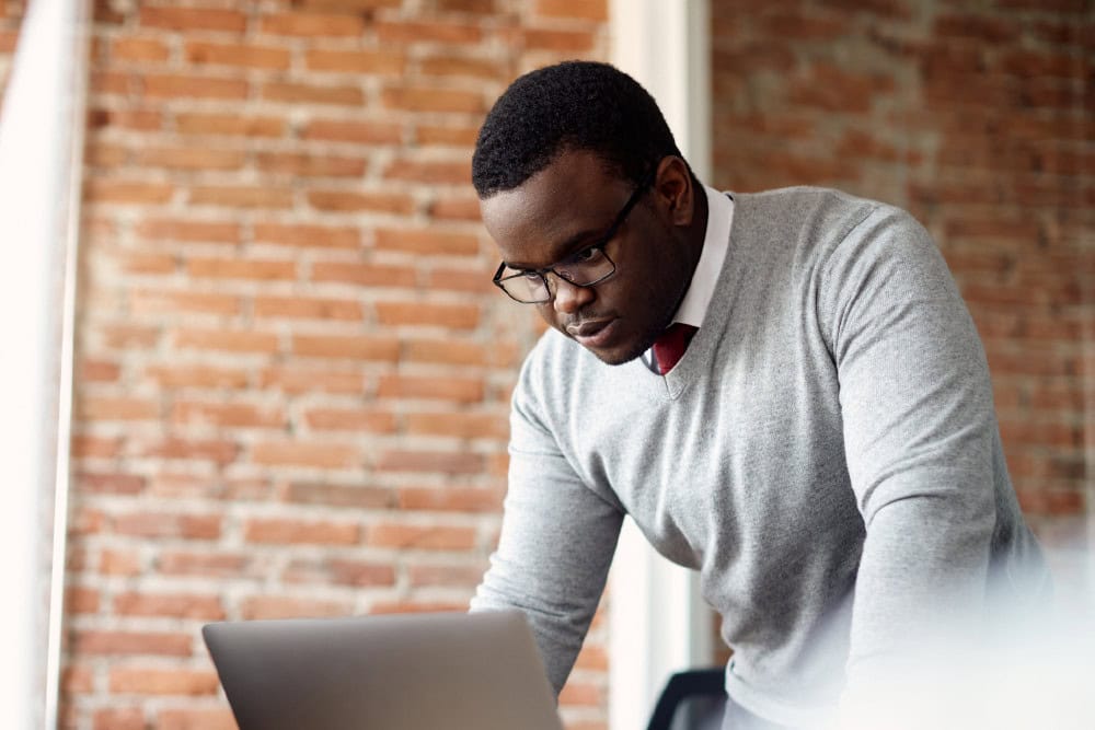 Business Studies: Adult student with laptop. Man in glasses studying business, brick wall background.