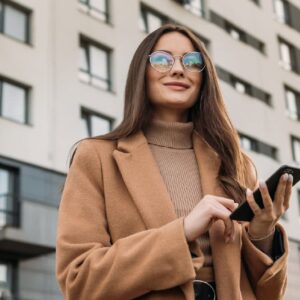 Adult matric English home language banner: Woman with phone, wearing coat and glasses.