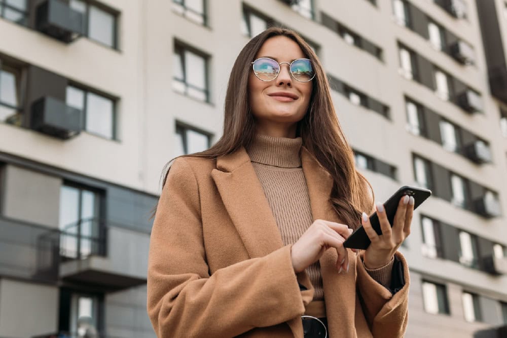 Adult matric English home language banner: Woman with phone, wearing coat and glasses.