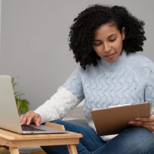 Woman studying online for Business Management Short Course. Laptop and clipboard on a desk.