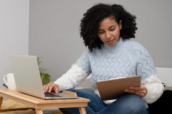 Woman studying online for Business Management Short Course. Laptop and clipboard on a desk.