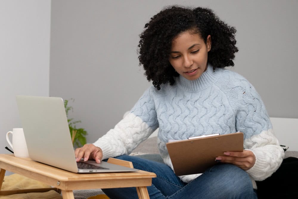Woman studying online for Business Management Short Course. Laptop and clipboard on a desk.