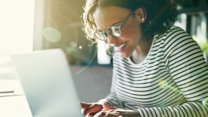 Happy telesales agent working on laptop. Woman smiling while using computer for commerce and sales.