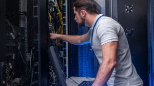 Application developer working on blockchain solutions architecture in a data center. Server rack with cables.