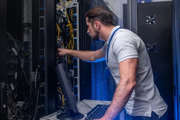 Application developer working on blockchain solutions architecture in a data center. Server rack with cables.