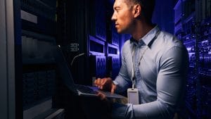 Apprentice developer working on servers. IT specialist with laptop in data center. Journeyman developer career.