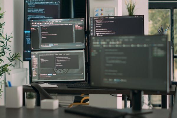 Network engineer's desk with multiple monitors displaying code. CloudOps, network security, and software development.