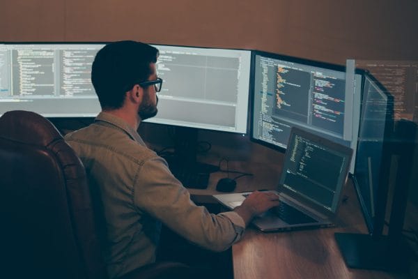 Programmer working on API development. Developer coding on multiple monitors.