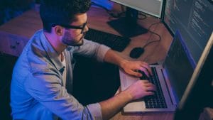 Agile programmer securing code. Man coding on laptop with multiple monitors. Software developer at work.