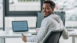 Security analyst to architect: Man at desk with laptop and monitor. Cybersecurity career advancement.