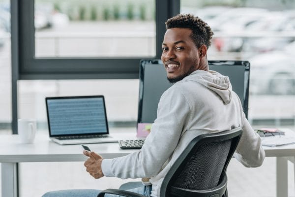 Security analyst to architect: Man at desk with laptop and monitor. Cybersecurity career advancement.