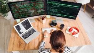 Software Tester to DevOps Automated Tester: Woman coding on dual monitors and laptop.