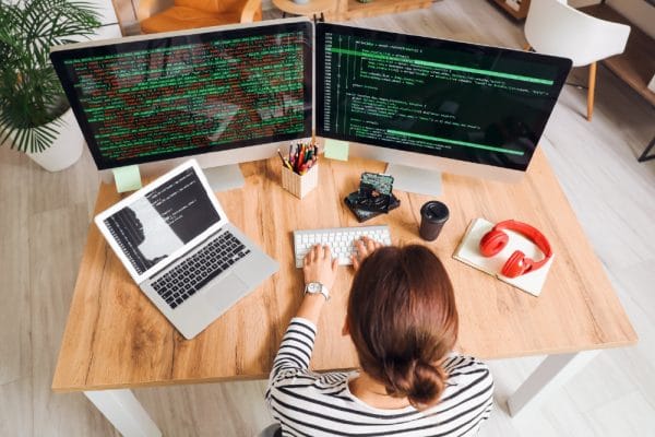 Software Tester to DevOps Automated Tester: Woman coding on dual monitors and laptop.