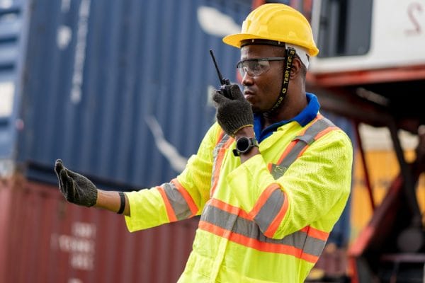 Occupational Health and Safety Representative. Worker with hard hat and safety vest using walkie-talkie at worksite.