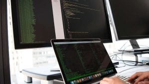 ISTQB CTFL: Software tester coding on laptop with dual monitors. Software testing, ISTQB certification.