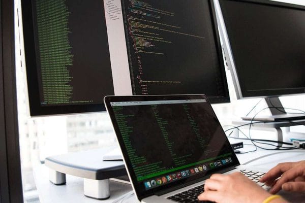 ISTQB CTFL: Software tester coding on laptop with dual monitors. Software testing, ISTQB certification.