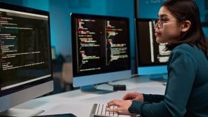 Woman coding PHP on multiple monitors. Learn PHP programming journey.