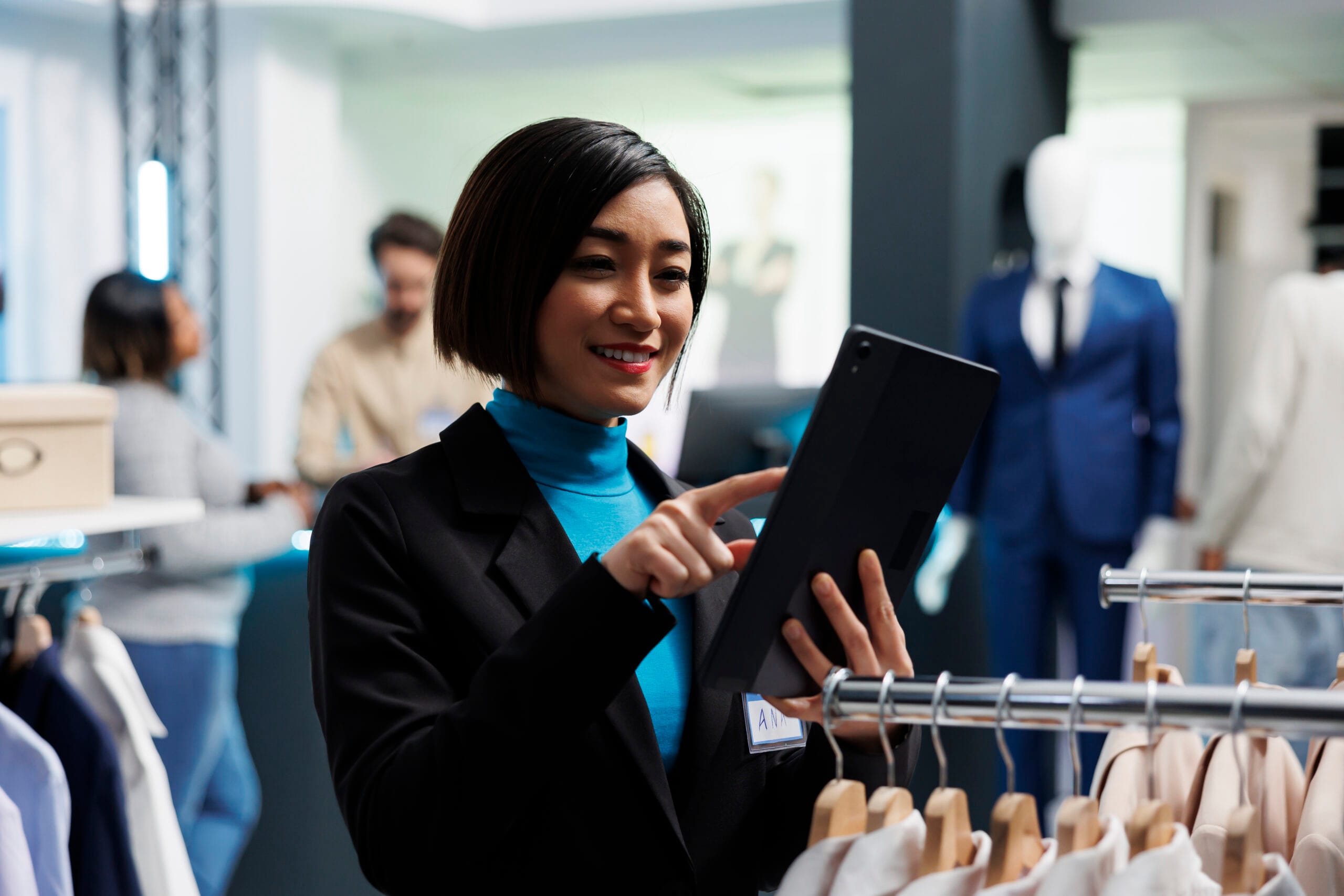 Merchandiser using tablet in store. Woman managing inventory, clothing racks. Retail merchandising journey.