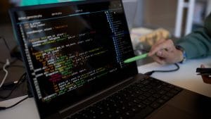 C++ programming: Laptop screen displays C++ code. A hand points to the code with a stylus. Focus on software development.