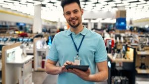 Smiling retail sales associate with tablet in electronics store. Employee journey.