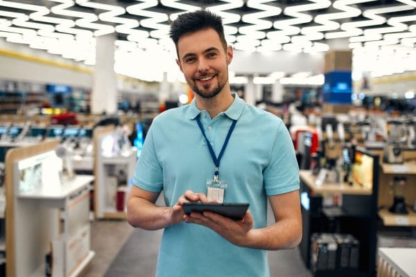 Smiling retail sales associate with tablet in electronics store. Employee journey.