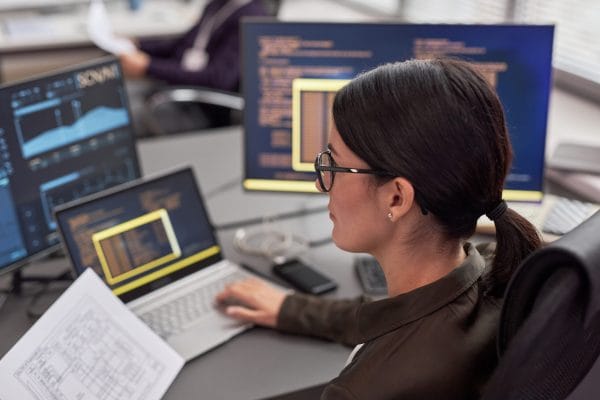 Security essentials: Woman analyzes data on multiple screens. Cybersecurity decision-makers use data to lead.