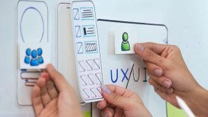 UI/UX design process. Hands arranging mobile app interface elements on a whiteboard. User experience planning.