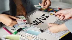 UX/UI design process. Hands arranging cards with app interface elements on a table. Brainstorming user experience.