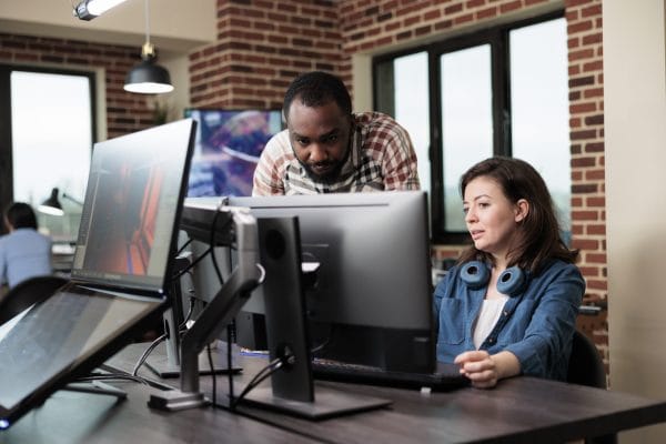 Windows desktop administration: Colleagues collaborate at computers in a modern office.