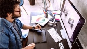 Graphic designer using Adobe bundle. Man with pen tablet, computer, and design tools. Creative workspace.