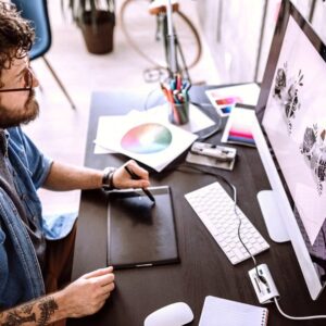Graphic designer using Adobe bundle. Man with pen tablet, computer, and design tools. Creative workspace.