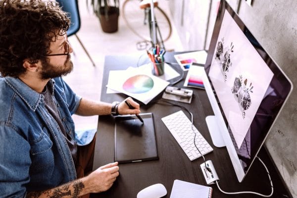 Graphic designer using Adobe bundle. Man with pen tablet, computer, and design tools. Creative workspace.