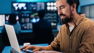 AWS Certified Developer Associate works on a laptop in front of monitors.