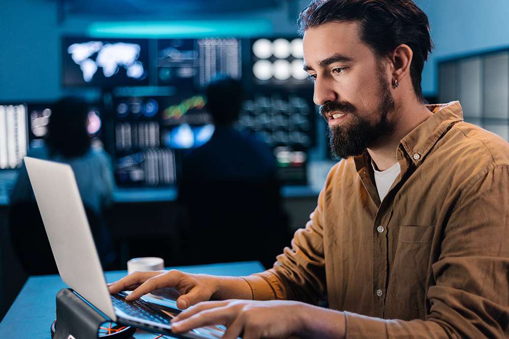 AWS Certified Developer Associate works on a laptop in front of monitors.