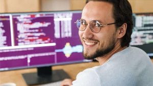 AWS Certified Solutions Architect: Man smiles at computer with code.