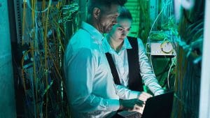 CompTIA Network+ professionals working on server. IT technicians with laptop in data center.