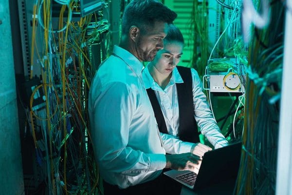 CompTIA Network+ professionals working on server. IT technicians with laptop in data center.