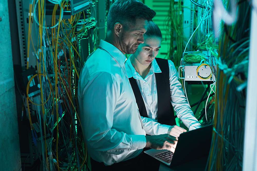 CompTIA Network+ professionals working on server. IT technicians with laptop in data center.