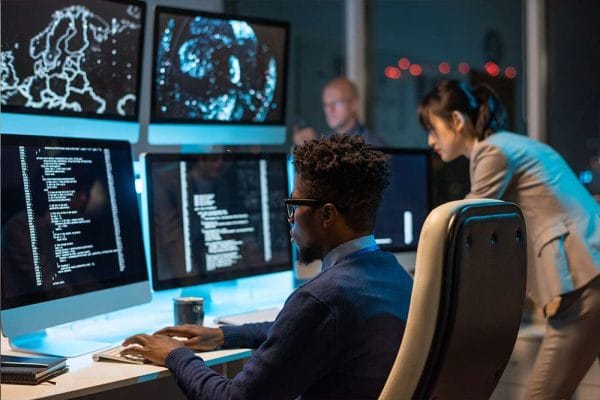 CompTIA PenTest+ team working. Cybersecurity professionals analyzing code on multiple monitors.