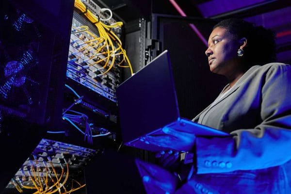 CompTIA Server+ candidate with laptop in data center. IT professional managing servers.